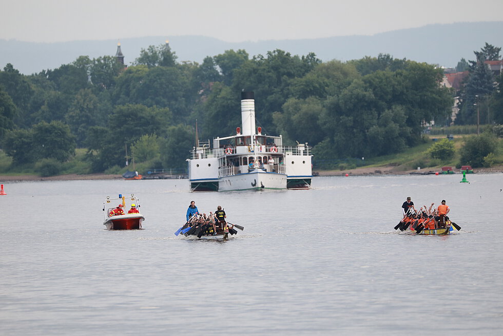 Zwei Drachenboote im ruhigen Gewässer im Hintergrund ein großes Dampfschiff mitten auf der Elbe