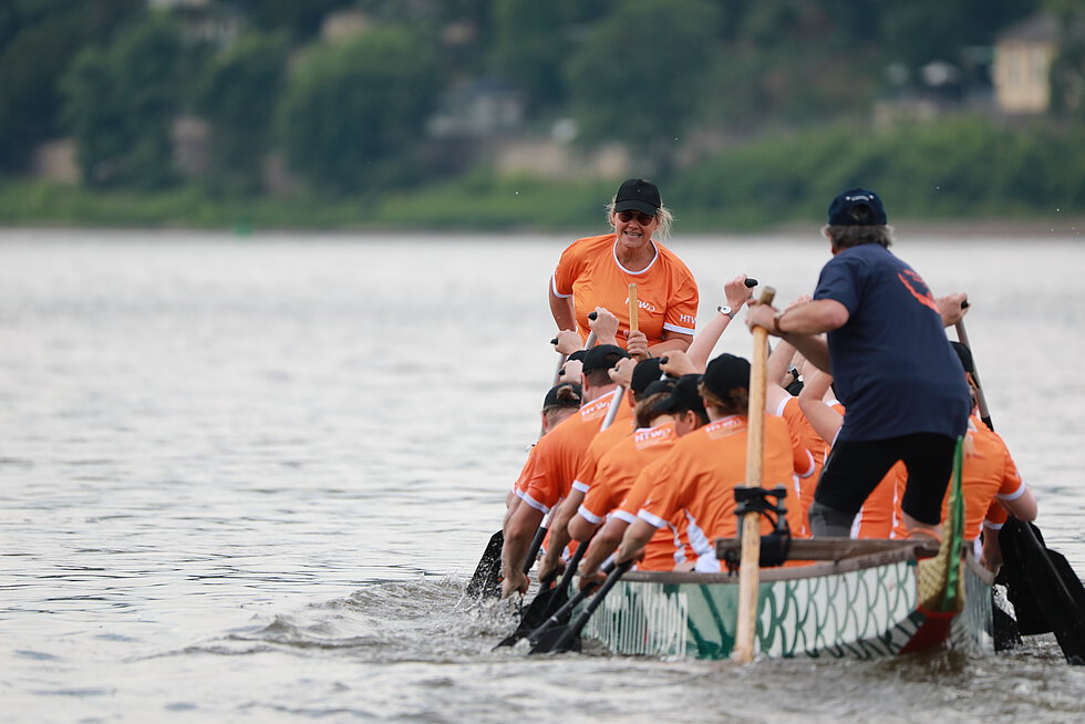 Ein bunt bemaltes Drachenboot mit Teammitgliedern in gleichfarbigen Outfits paddelt synchron über das Wasser.